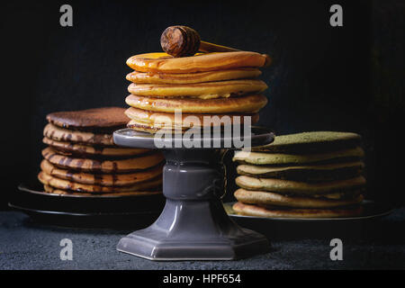 Auswahl an hausgemachten amerikanischen Ombre Schokolade, Grüntee Matcha und Kurkuma Pfannkuchen mit Honig und Sauce serviert auf Platten und Kuchen über schwarz s stehen Stockfoto