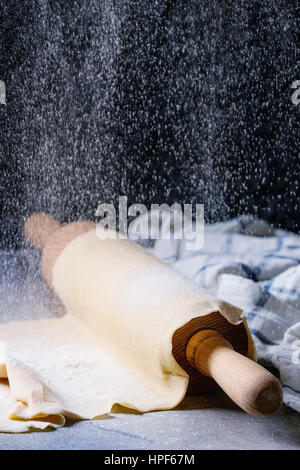 Frische hausgemachte Teig für Nudeln Tagliatelle auf Holz Nudelholz mit Sieb Prise Mehl und Küche Handtuch über dunklen grauen Tabellenhintergrund gerollt. Stockfoto