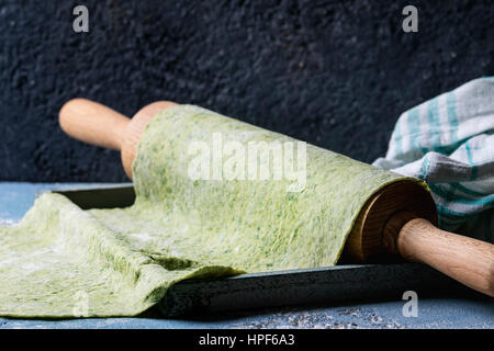 Frische hausgemachte Grüne Spinat Teig für Nudeln Tagliatelle auf Holz Nudelholz mit Ei Eigelb und Küche Handtuch über dunkelgrauen Hintergrund gerollt. Top vie Stockfoto