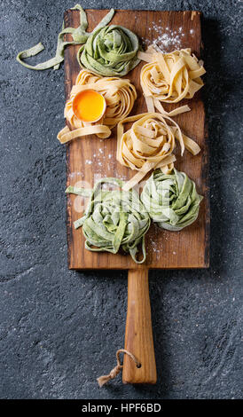 Verschiedene farbige frische rohe hausgemachte Teigwaren Tagliatelle grün Spinat und traditionellen gelb mit Eigelb auf Holzbrett über dunkel Stockfoto