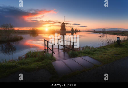 Silhouette von Windmühlen bei nebligen Sonnenaufgang in Kinderdijk, Niederlande. Rustikale Landschaft mit Holzsteg gegen holländische Windmühlen in der Nähe der Grachten Stockfoto