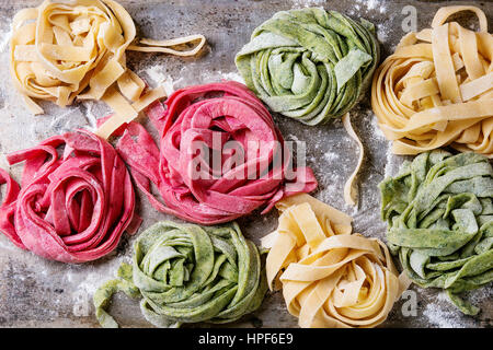 Vielzahl von farbigen frischen rohen hausgemachte Teigwaren Tagliatelle grün Spinat, rosa rote Beete und gelb mit Mehl über alte Metall Textur Hintergrund.