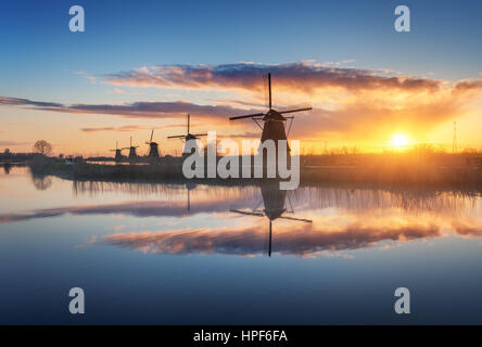 Silhouette von Windmühlen bei erstaunlichen nebligen Sonnenaufgang in Kinderdijk, Niederlande. Rustikale Landschaft mit holländischen Windmühlen in der Nähe der Kanäle und bunten Himmel Stockfoto