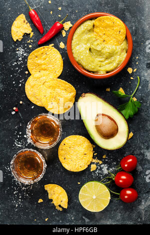 Schüssel mit mexikanische Nachos chips mit hausgemachten frischen Guacomole Sauce und Tequila Shots über alte Hintergrund. Ansicht von oben. Mit Platz für text Stockfoto