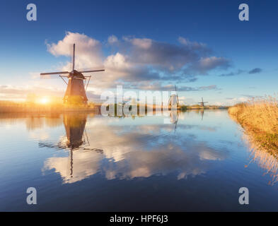 Windmühlen bei Sonnenaufgang. Rustikale Landschaft mit erstaunlichen holländische Windmühlen in der Nähe der Wasserkanäle mit blauen Himmel und Wolken spiegeln sich in Wasser Stockfoto
