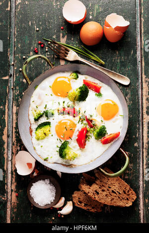Pfanne mit gebratenen Eiern, Brokkoli und Tomaten mit Brot auf alten grünen Hintergrund, Ansicht von oben Stockfoto