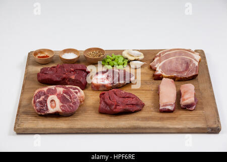 Sorten von Fleisch mit Gewürzen auf Holzbrett vor weißem Hintergrund Stockfoto