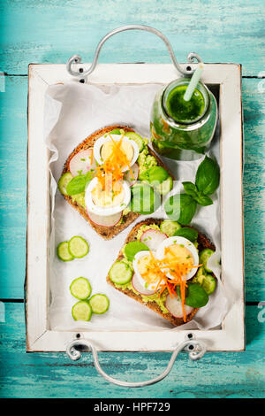 Gesunde vegetarische Sandwiches (mit Avocado, Tomate, Gurke, Zwiebel, rote Beete, Frischkäse, Kräuter und Gewürze) auf blauem Hintergrund rustikal Stockfoto