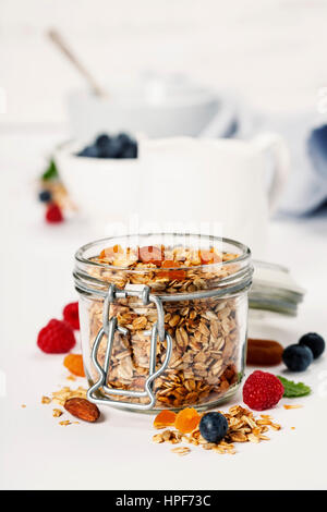 Hausgemachtem Müsli (mit getrockneten Früchten und Nüssen) und gesundes Frühstückszutaten - Honig, Milch und Beeren auf weißem Hintergrund Stockfoto