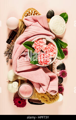 Spa-Hintergrund mit Meersalz, Schüssel, Blumen, Wasser, Seife, Kerzen, ätherische Öle, massage-Bürste und Blumen, Ansicht von oben. Flach zu legen. Rosa Hintergrund Stockfoto