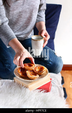 Weiblich, Frühstück im Bett. Portugiesischer Pudding Kuchen mit einer Tasse Kaffee Stockfoto