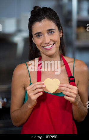 Porträt von lächelnden Mitarbeiterinnen zeigen Herz Form Cookie am Schalter in der Backstube Stockfoto