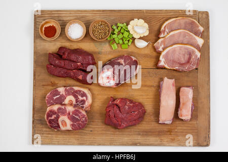 Sorten von Fleisch mit Gewürzen auf Holzbrett vor weißem Hintergrund Stockfoto