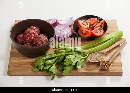 Hackfleisch und Zutaten auf Holzbrett vor weißem Hintergrund Stockfoto