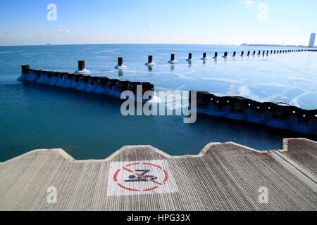 "Kein Schwimmen' Schild am Seeufer entlang mit Blick auf Holz- Beiträge neben den Horizont und die Skyline von Chicago in einem eisigen See Michigan im Winter Stockfoto