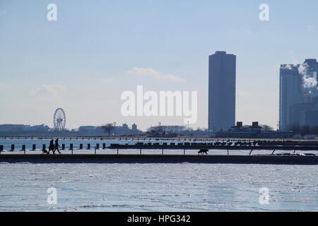 Fußgänger und Hunde Spaziergang am Pier ragt in einen zugefrorenen See, Michigan mit den großen Skyline von Chicago und den Navy Pier Attraktion den backgroun Stockfoto