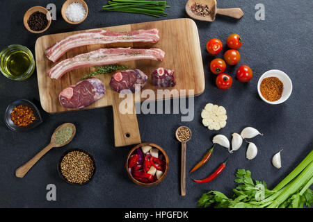 Sorten von Fleisch mit Gewürzen auf Holzbrett vor schwarzem Hintergrund Stockfoto