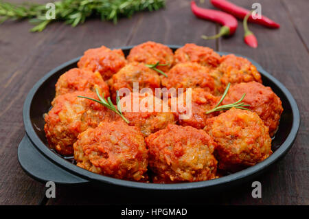 Fleischbällchen in würziger Tomatensauce serviert in einer gusseisernen Pfanne auf einem dunklen Hintergrund aus Holz. Stockfoto
