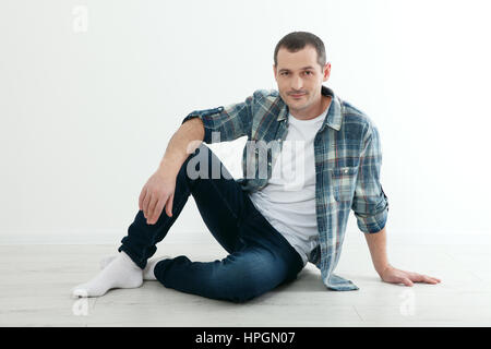 Glückliche Menschen sitzen auf dem Boden in der Nähe einer weißen Wand in seinem neuen Haus auf weißem Hintergrund Stockfoto