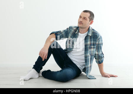 Glückliche Menschen sitzen auf dem Boden in der Nähe einer weißen Wand in seinem neuen Haus auf weißem Hintergrund Stockfoto