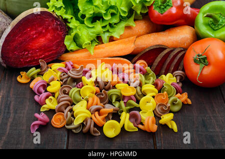 Bunte Nudeln auf einem dunklen rustikalen Holztisch mit frischem Gemüse (Rüben, Grüns, Karotten, Tomaten, Paprika). Gesunde Ernährung-Konzept. Stockfoto