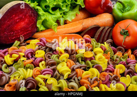 Bunte Nudeln auf einem Tisch mit frischem Gemüse (Rüben, Grüns, Karotten, Tomaten, Paprika). Gesunde Ernährung-Konzept. Nahaufnahme Stockfoto