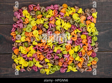 Bunte Nudeln mit Gemüse (Rüben, Grüns, Spinat, Karotten, Tomaten, Paprika) auf einem dunklen Holztisch gefärbt. Gesunde Ernährung-Konzept. Die Ansicht von oben Stockfoto