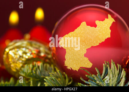 Eine glänzende rote Christbaumkugel mit der goldenen Form von Nordkorea. (Serie) Stockfoto