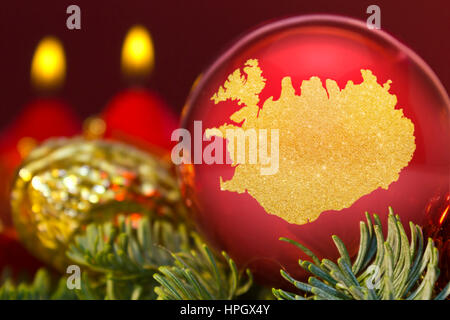 Eine glänzende rote Christbaumkugel mit der goldenen Form von Island. (Serie) Stockfoto