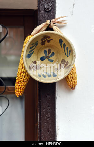 Dekorative rustikale Keramikplatte und Mais auf einer weißen Wand hängen Stockfoto
