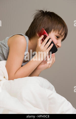 Junge Mit praktisch Im Bett - junge mit Mobile im Bett, veröffentlichte Modell Stockfoto
