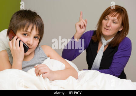 Sohn Im Bett Mit Handy, Schimpft Mutter - Sohn mit Handy im Bett, Mutter schimpft, Modell veröffentlicht Stockfoto