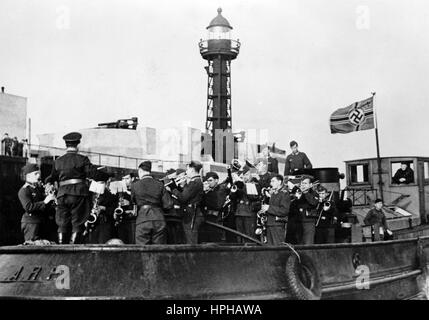 Das Bild der Nazi-Propaganda zeigt deutsche Wehrmachtssoldaten in einem Hafen an der Kanalküste im besetzten Frankreich. Veröffentlicht im Oktober 1940. Ein Nazi-Reporter hat auf der Rückseite des Bildes auf 07.02.1942 geschrieben: "Eine glückliche Überraschung für unsere Soldaten an der Kanalküste. Eine Marschkapelle der Luftwaffe spielt auf einem Hafendampfboot, so sicher wie eine erfahrene Marschkapelle. Auf diese Weise können sie alle Genossen in den Stützpunkten rund um den Kanalhafen mit ihrem Standkonzert erreichen." Fotoarchiv für Zeitgeschichte - KEIN KABELDIENST - | weltweite Nutzung Stockfoto