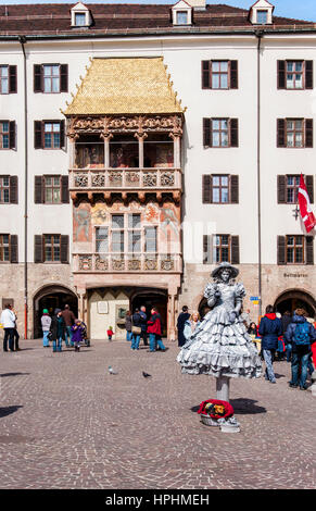 INNSBRUCK, Österreich - 20. März 2010: Goldenes Dachl (Goldenes Dachl) in Innsbruck, Österreich, und eine weibliche Straßenmusiker, die Durchführung einer lebenden Statue aus Stein Stockfoto