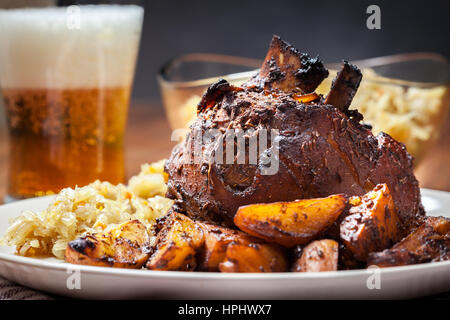 Schweinshaxe mit gebratenem Sauerkraut und Bratkartoffeln auf einem Teller Stockfoto