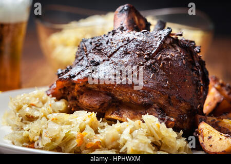 Schweinshaxe mit gebratenem Sauerkraut und Bratkartoffeln auf einem Teller Stockfoto