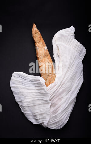 Französisches Baguette oder Bauernbrot in weißen Handtuch gewickelt auf schwarzem Hintergrund. Ansicht von oben. Stockfoto