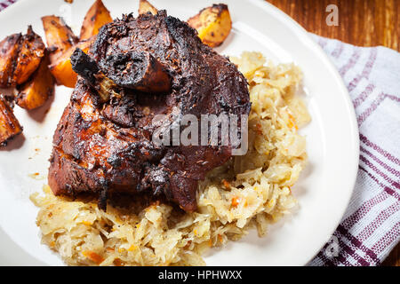 Schweinshaxe mit gebratenem Sauerkraut und Bratkartoffeln auf einem Teller Stockfoto