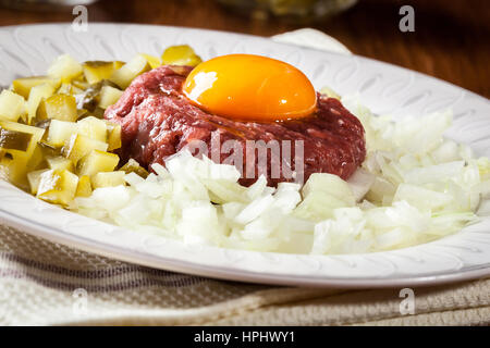 Steak Tartar mit Eigelb, Zwiebeln und Gurken auf einem Teller Stockfoto