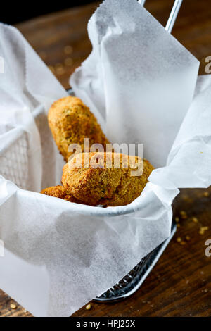 einige hausgemachte Croquetas, spanische Kroketten, serviert in einem Metallkorb, platziert auf einem rustikalen Holztisch Stockfoto