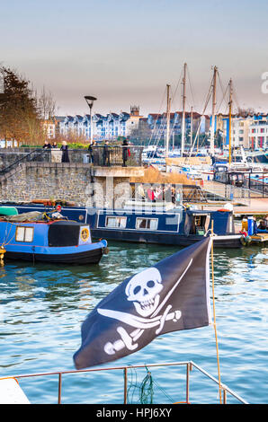 Ein Boot fliegt die Piratenflagge im Vordergrund, während Narrowboats hinter, in dieser Szene der Hafen von Bristol, UK festgemacht sind Stockfoto