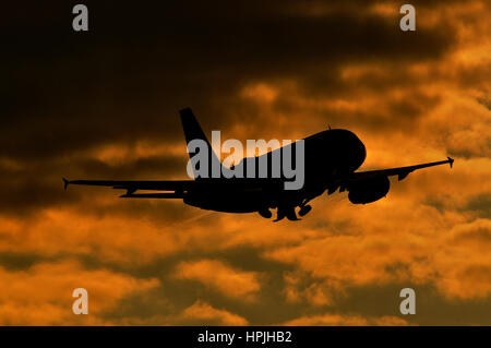 Silhouette des Airbus A319 (kürzere Version des A320) Passagier-Jet im Sonnenuntergang mit Orange beleuchteten Wolken im Hintergrund Stockfoto