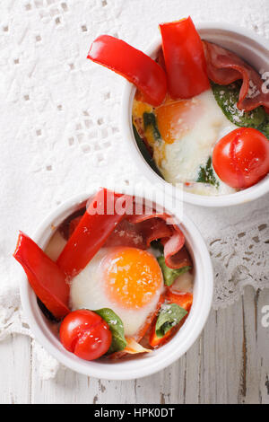 Spiegelei mit Spinat, Paprika, Tomaten und Käse in eine Tasse Nahaufnahme auf dem Tisch. vertikale Ansicht von oben Stockfoto