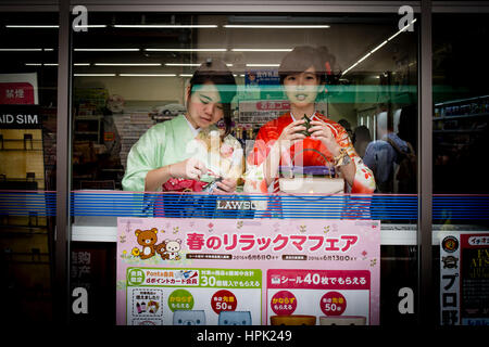 Zwei junge Frauen in Kimono Essen und Snacks in einem Lebensmittelgeschäft, Kyoto, Japan Stockfoto