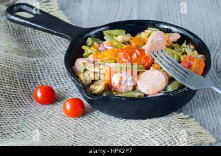 Gebratenes Gemüse mit gehackten Wurst in einem gusseisernen Pfanne ein Stück auf einer Gabel. Graues Holz Hintergrund, Sackleinen und selektiven Fokus. Stockfoto