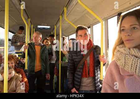 Verschiedene Menschen können gesehen werden, stehen und sitzen in einem Bus. Einige sprechen, andere sind aus dem Fenster schaute. Stockfoto