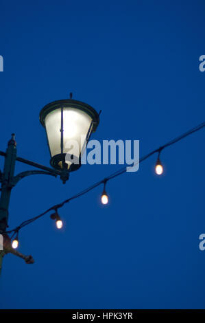 Straßenlaterne und Lichterkette gegen Himmel verdunkeln Stockfoto