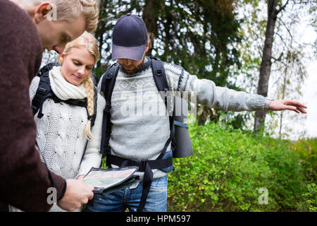 Junge männliche und weibliche Wanderer diskutieren über Karte im Wald Stockfoto