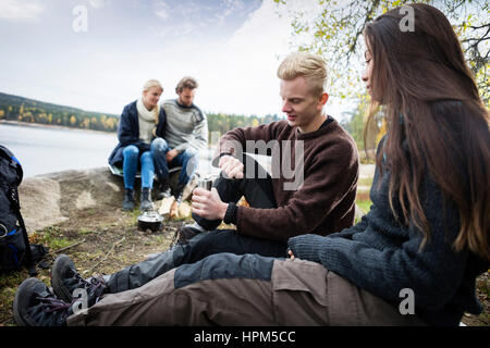 Junges Paar Mahlen des Kaffees mit Freunden im Hintergrund am Seeufer beim camping Stockfoto