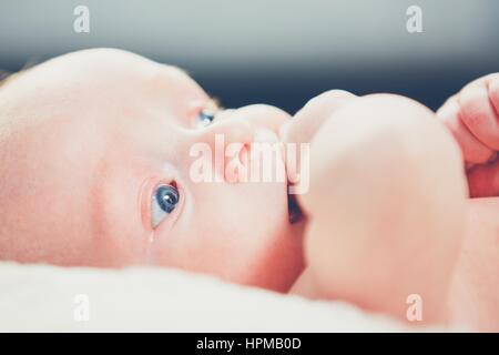 Kleines Baby mit blauen Augen und Hand in den Mund. Stockfoto